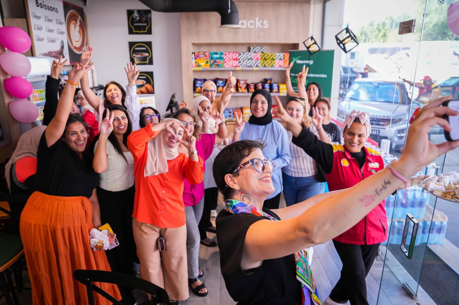 In a modern service station, a group of Tunisian women smile and pose for a selfie.