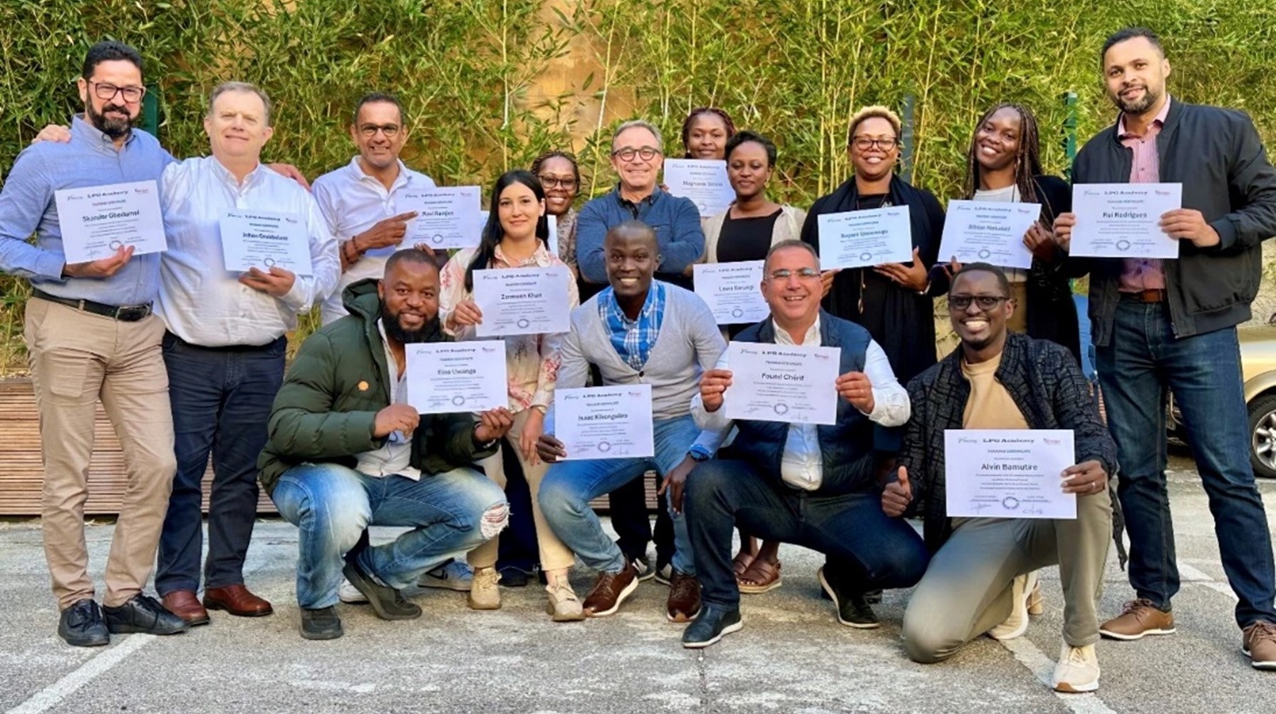 Group of people pose in front of a green hedge, holding white certificates