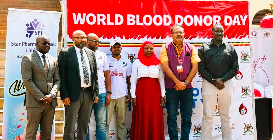 Representatives of the partner companies stand in front of a red World Blood Donor Day banner